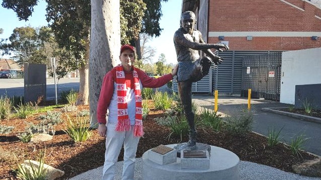 A man wearing a red and white Swans scarf next to a statue of a man kicking a ball