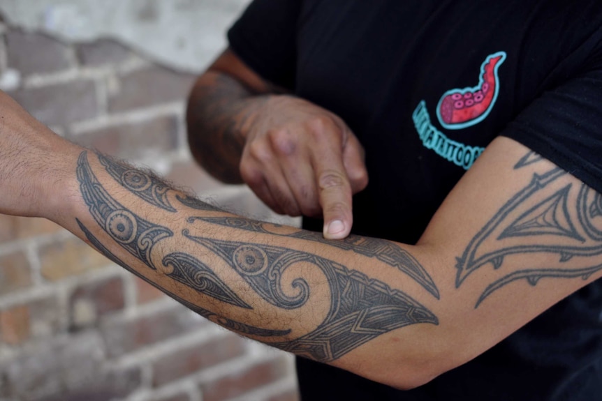A Maori man whose face is not in shot points at a traditional tattoo on his arm, explaining its meaning.