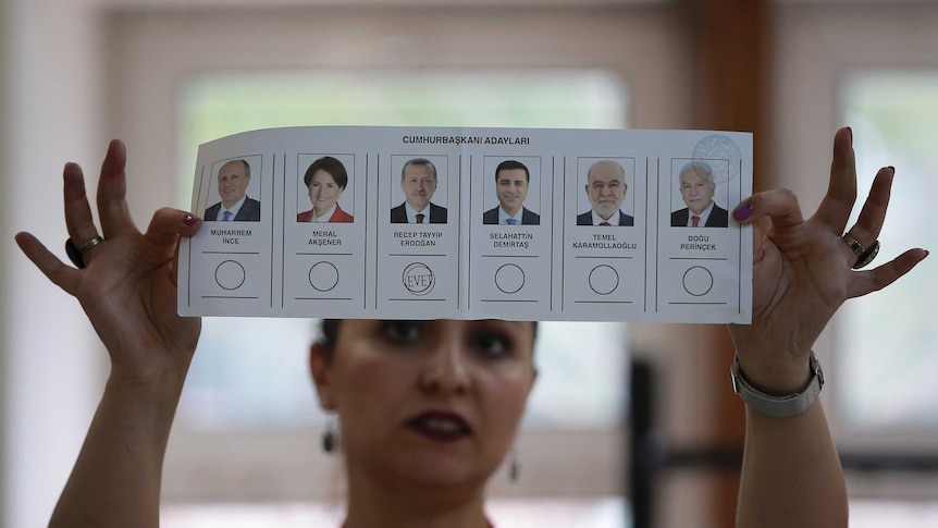 A lady holds up a voting card with pictures of candidates and a stamp under Erdogan's photo