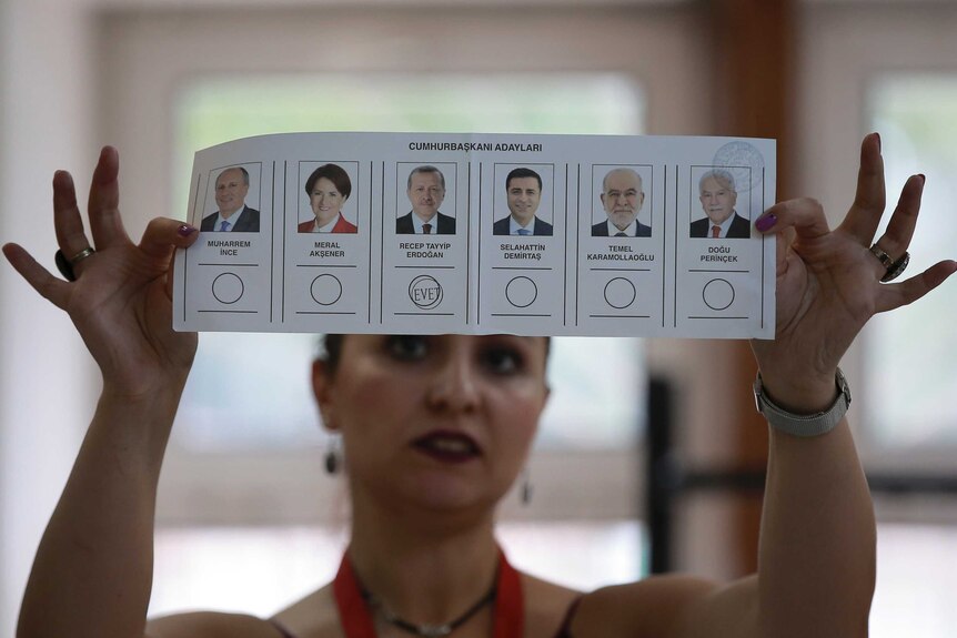 A lady holds up a voting card with pictures of candidates and a stamp under Erdogan's photo