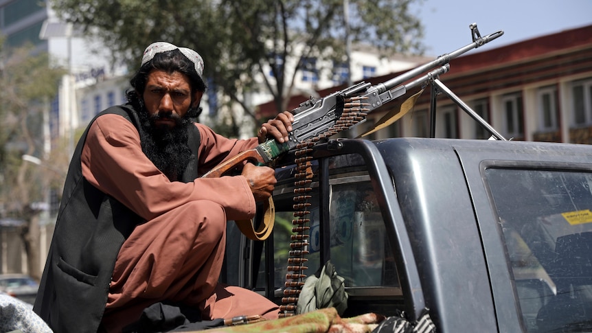 A man sits on the back of a ute with a gun and several rounds of ammunition