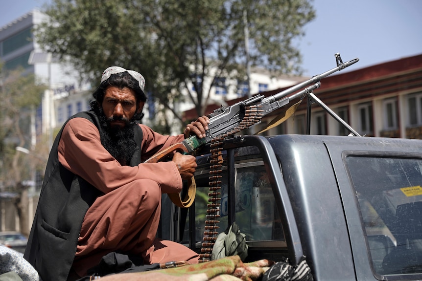 A man sits on the back of a ute with a gun and several rounds of ammunition
