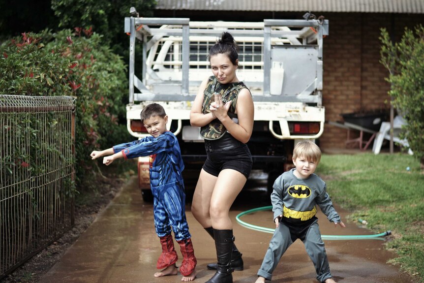 Mum and two children in dress ups pose in driveway.
