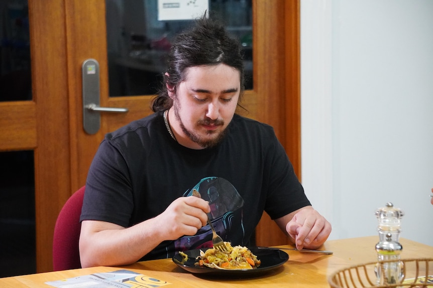 A photo of a young man wearing a black t-shirt eating noodles