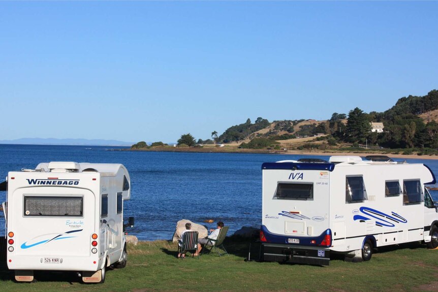 A couple look out over a beach sitting next to two motorhomes.