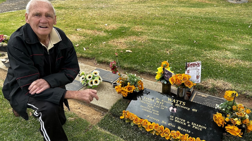 a man at a tombstone surrounded by flowers 