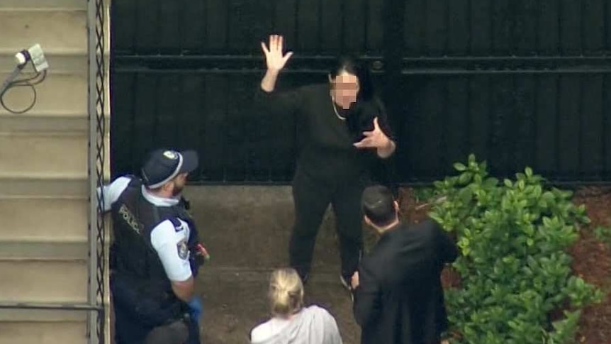 A woman surrounded by police officers, waving her hands in the air.