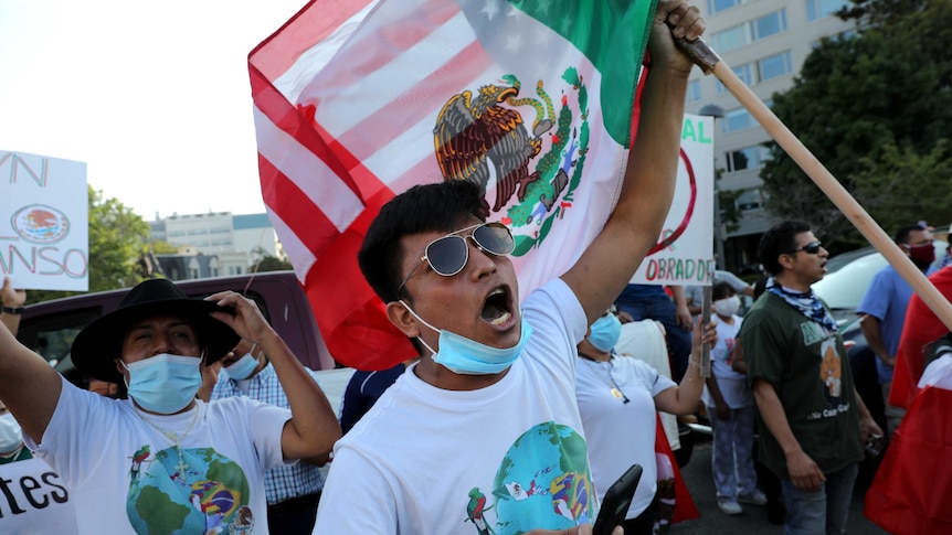 A man wearing a face mask around his chin appears to be yelling while waving a Mexican flag