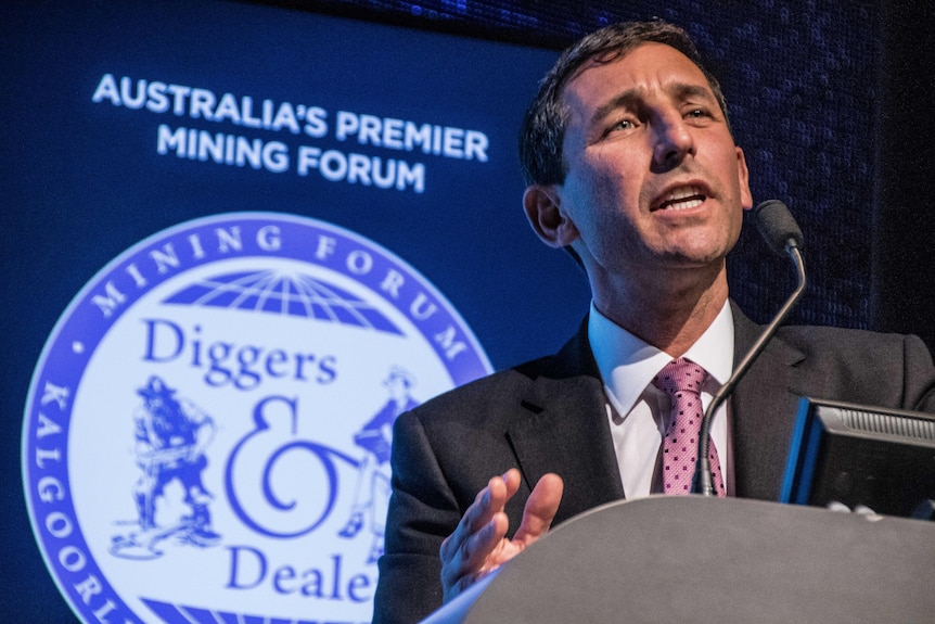 A man wearing a suit and tie speaking at a podium at a mining conference.  