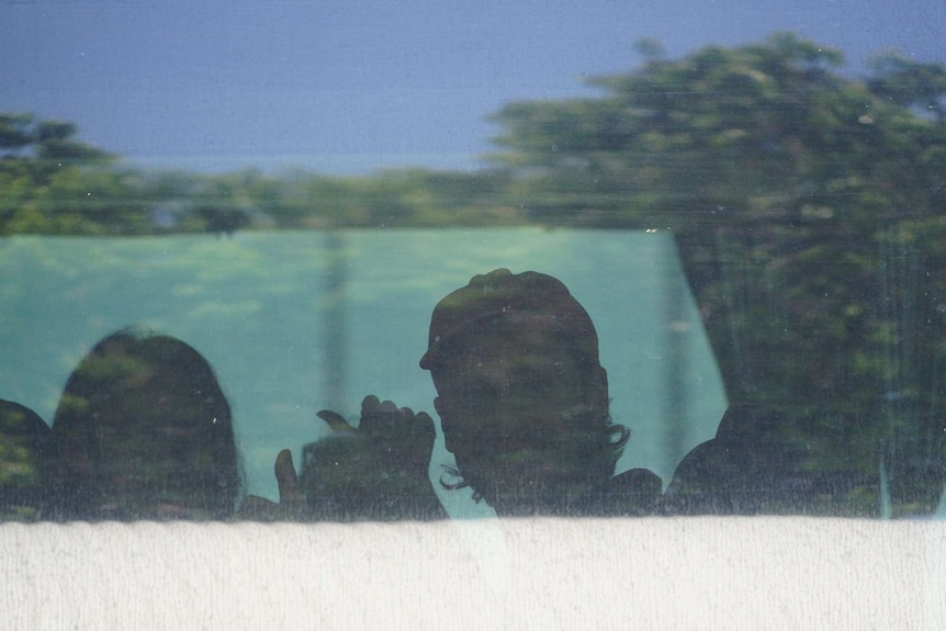 A man in a cap smiles through a bus window.