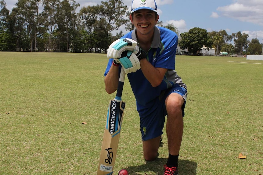 A man kneels on a green cricket field holding a cricket bat. Ausnew Home Care, NDIS registered provider, My Aged Care