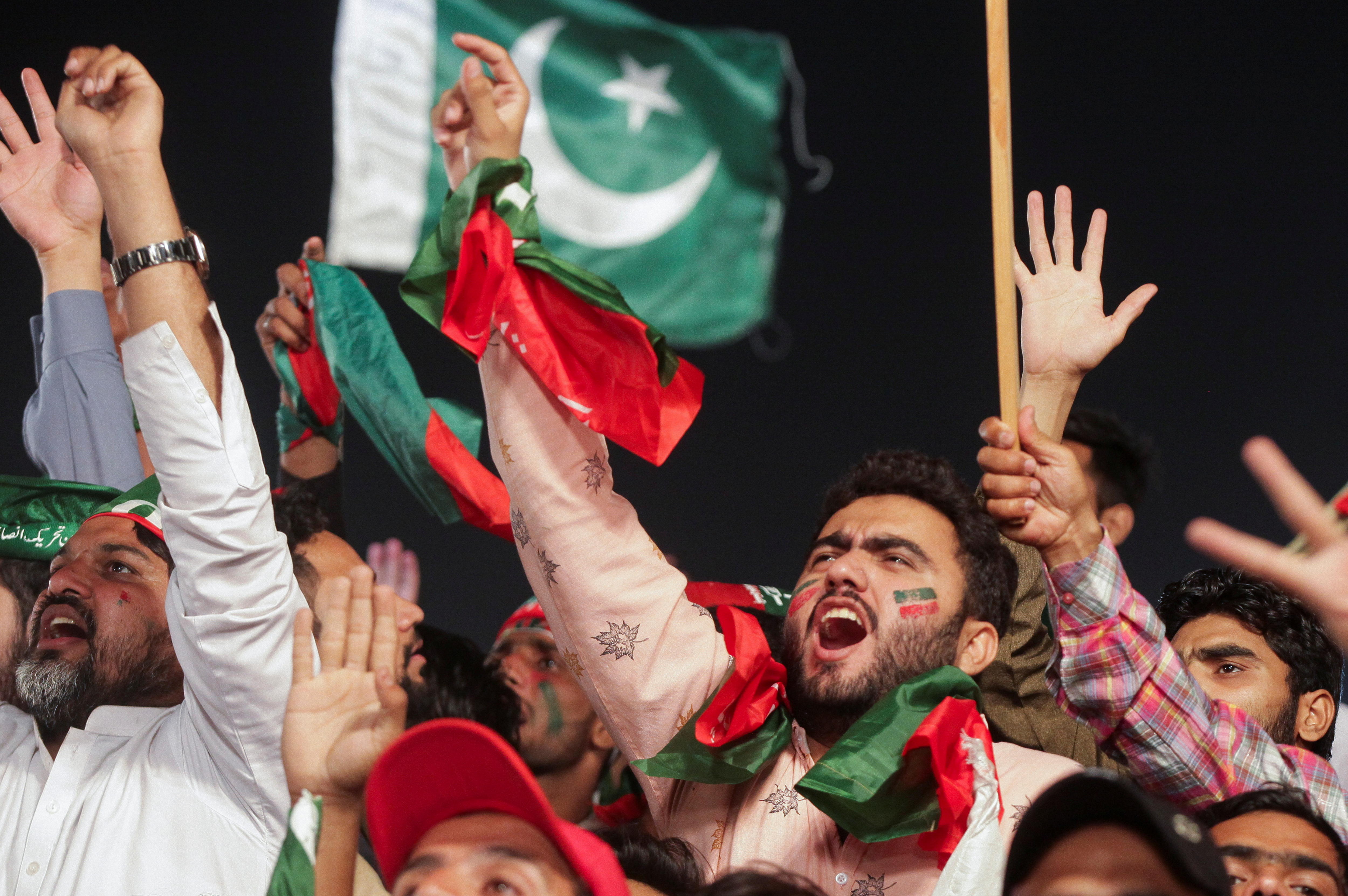 men wearing Pakistani flags throw their hands in the air and wave in support.