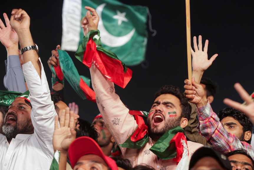men wearing Pakistani flags throw their hands in the air and wave in support.