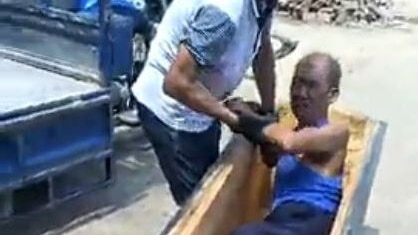 Still from a video showing a man in a coffin, and another man trying to pull him out.