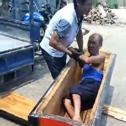 Still from a video showing a man in a coffin, and another man trying to pull him out.