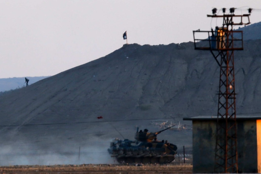 An Islamic State fighter walks near a black flag belonging to the Islamic State near Kobani