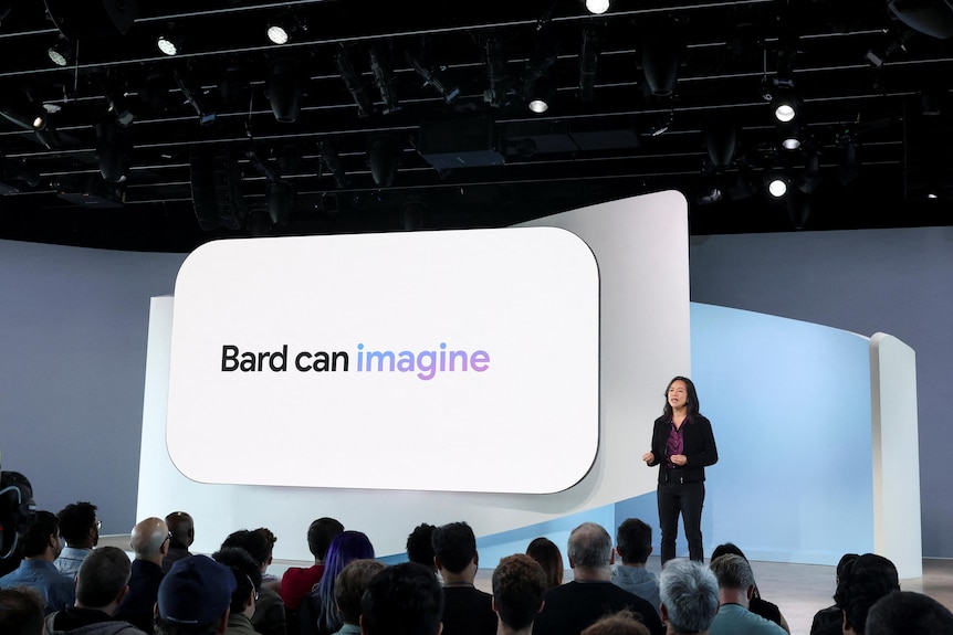 A woman stands on stage next to a screen with the words Bard can imagine