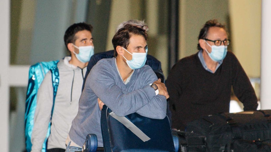 Rafael Nadal wears a mask and leans on a baggage carousel