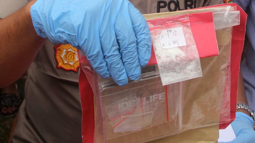 A Bali police officer holds up small bags of drugs in his blue-latex-gloved hand.