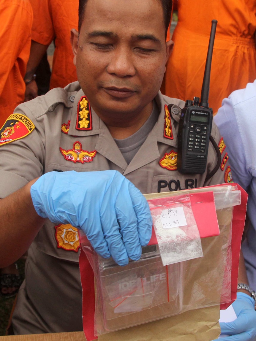A Bali police officer holds up small bags of drugs in his blue-latex-gloved hand.