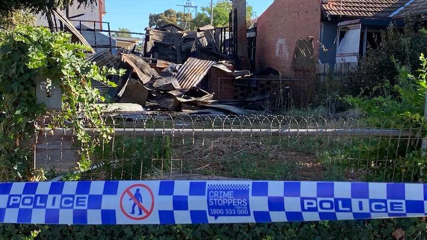 Burnt rubble of a house behind police tape.