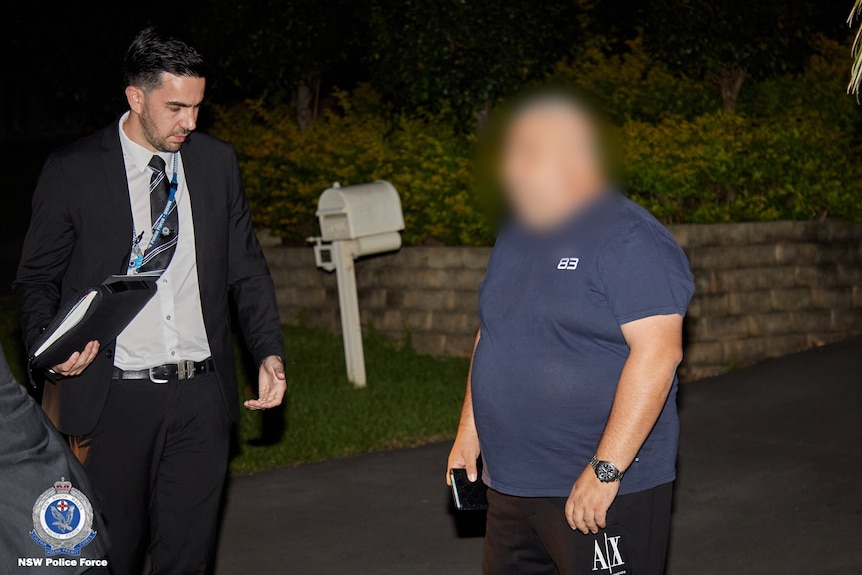  a man standing with his face blurred outside a home next to a police officer