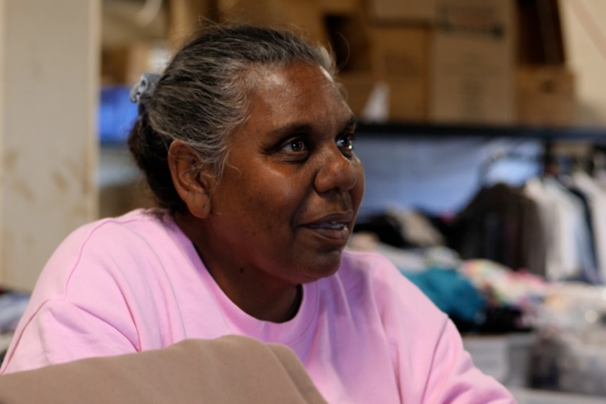 A woman in a pink jumper with black and grey hair in an op shop