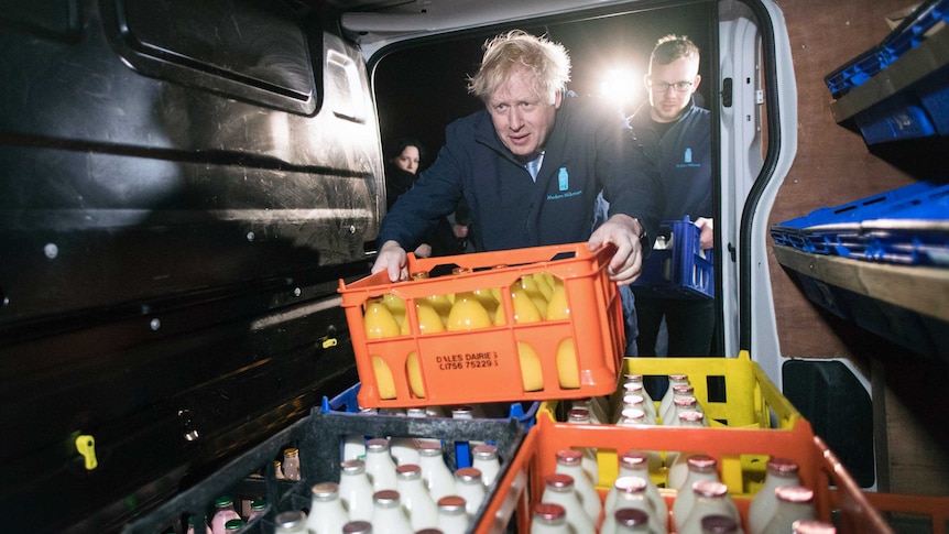 British PM Boris Johnson leans into the back of a cold drink delivery van, grabbing a crate full of juice bottles.