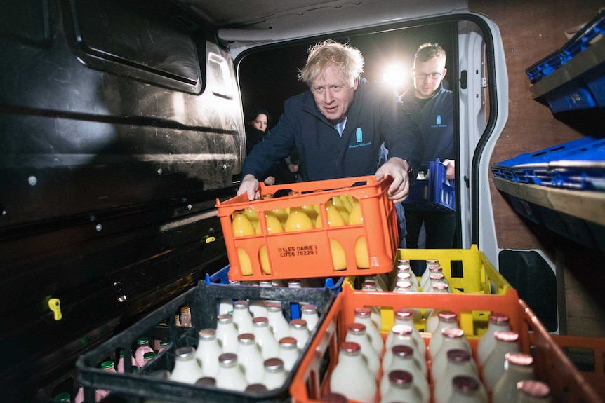 British PM Boris Johnson leans into the back of a cold drink delivery van, grabbing a crate full of juice bottles.