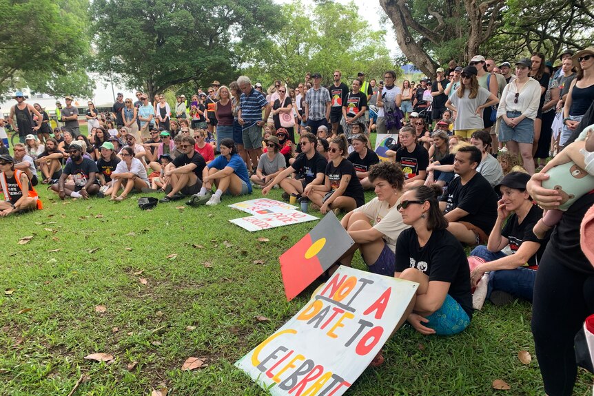 Crowd of people sit on grass with rally signs