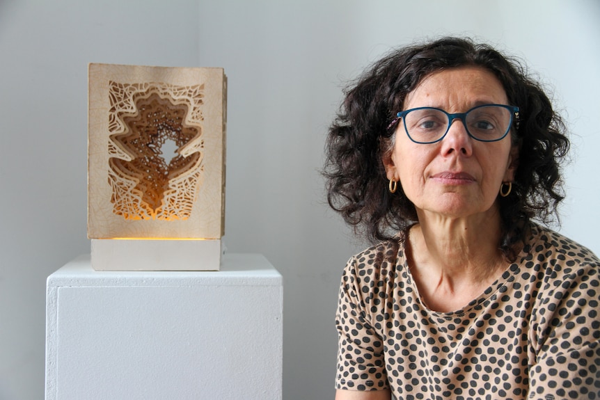 A woman sits in front of her artwork 