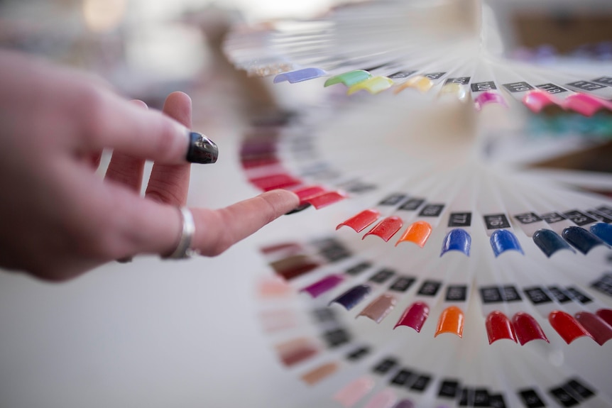 A hand touching nail polish colours in a salon.