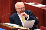 Federal Attorney-General George Brandis yawns while reading a document in the Senate.