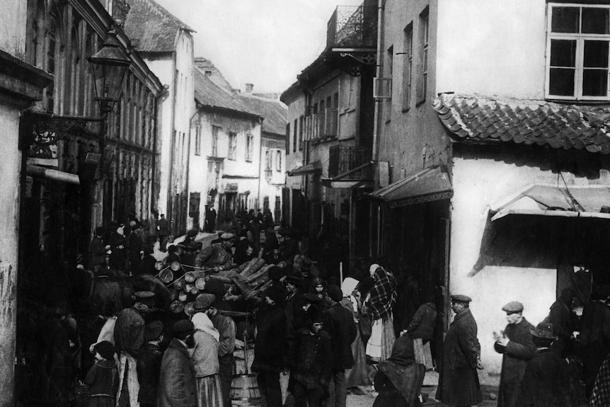 A black and white photograph shows shoppers milling about in the meat market alley in Eastern Europe in 1918.