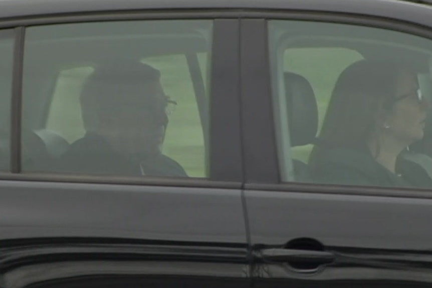 George Pell is seated in the back of a black car being driven along a road.
