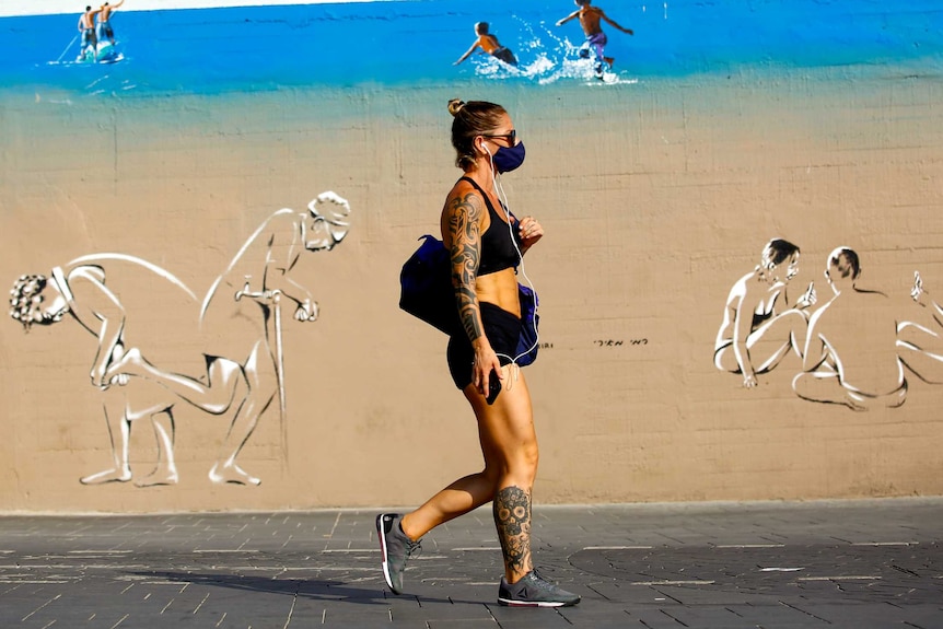 A woman in a face mask walks past a bright painted mural