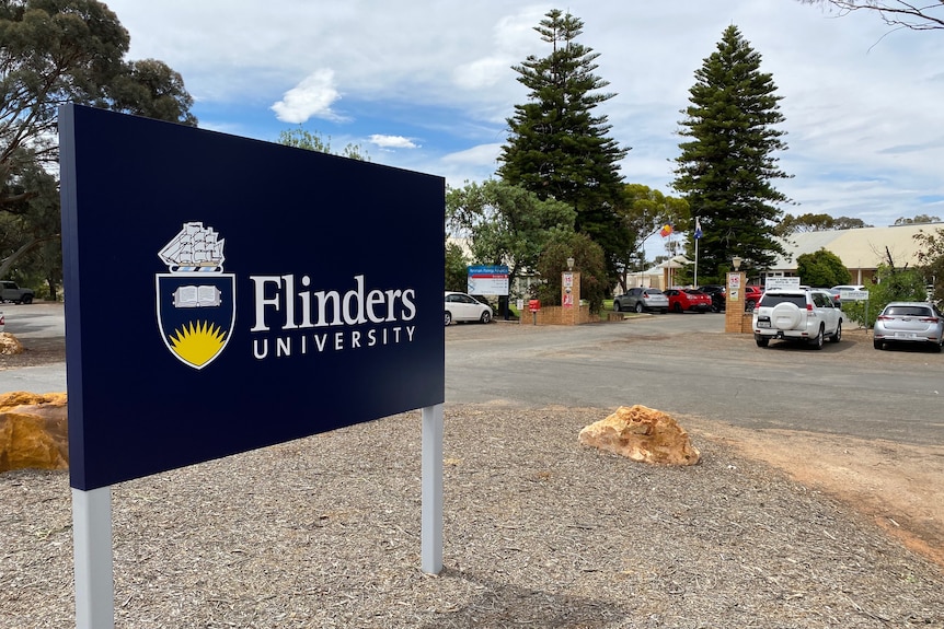 A blue sign out the front of a building which reads "Flinders University". 