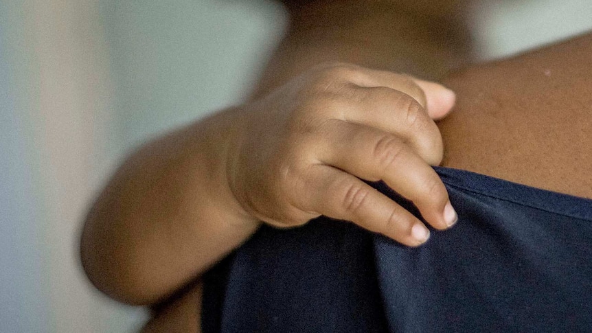 A baby's hand rests on her mother's shoulder