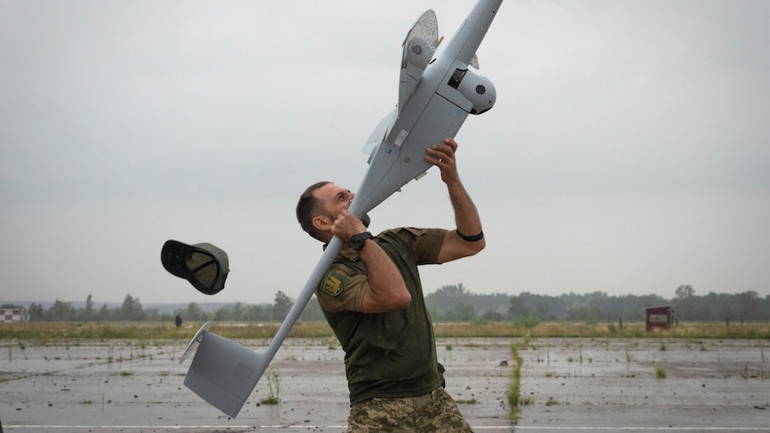 A Ukrainian soldier launches a drone over his shoulder as his cap flies off. 