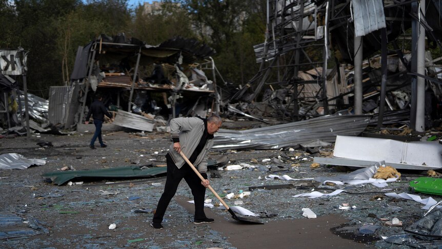 A man shovels the ground covered in debris. 
