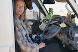 Brie Dickson sits in the front seat of her landcruiser with her brown dog peeking through the back. 