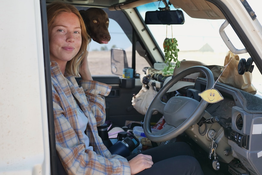 Brie Dickson sits in the front seat of her landcruiser with her brown dog peeking through the back. 