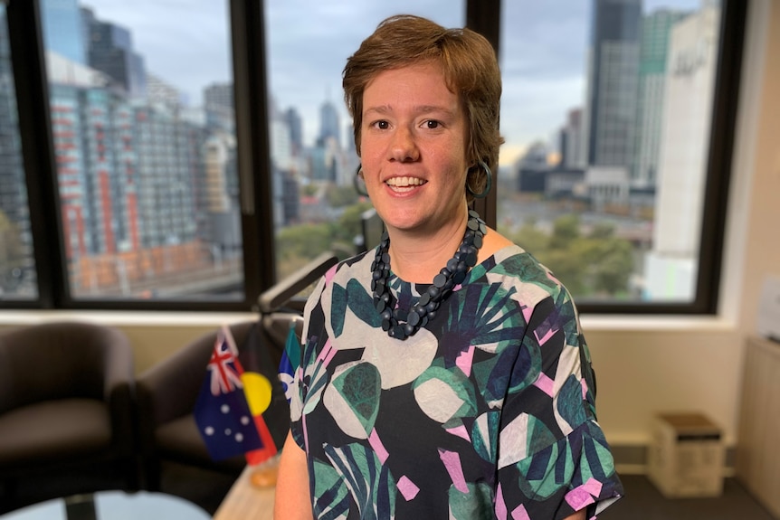 Lauren Cordwell from RWAV sits in front of a window, with small Australian and Aboriginal flags on table  behind her.