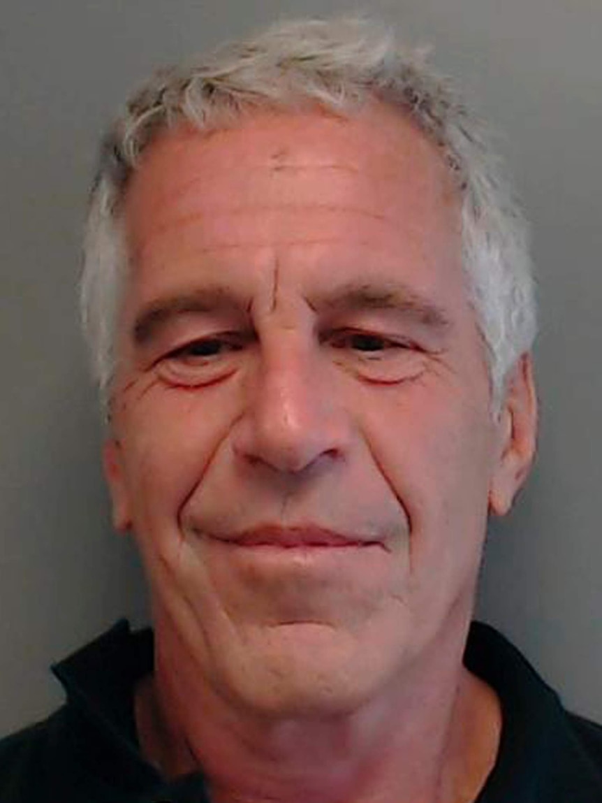 Jeffrey Epstein smiles at the camera in front of a grey background.