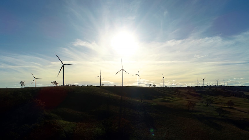 A group of wind turbines are silhouetted against the sky at sunset.