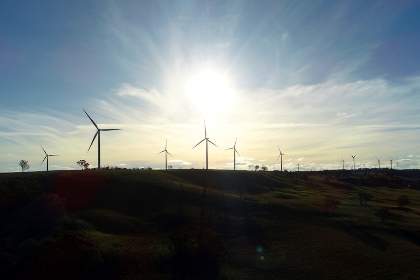 A group of wind turbines are silhouetted against the sky at sunset.