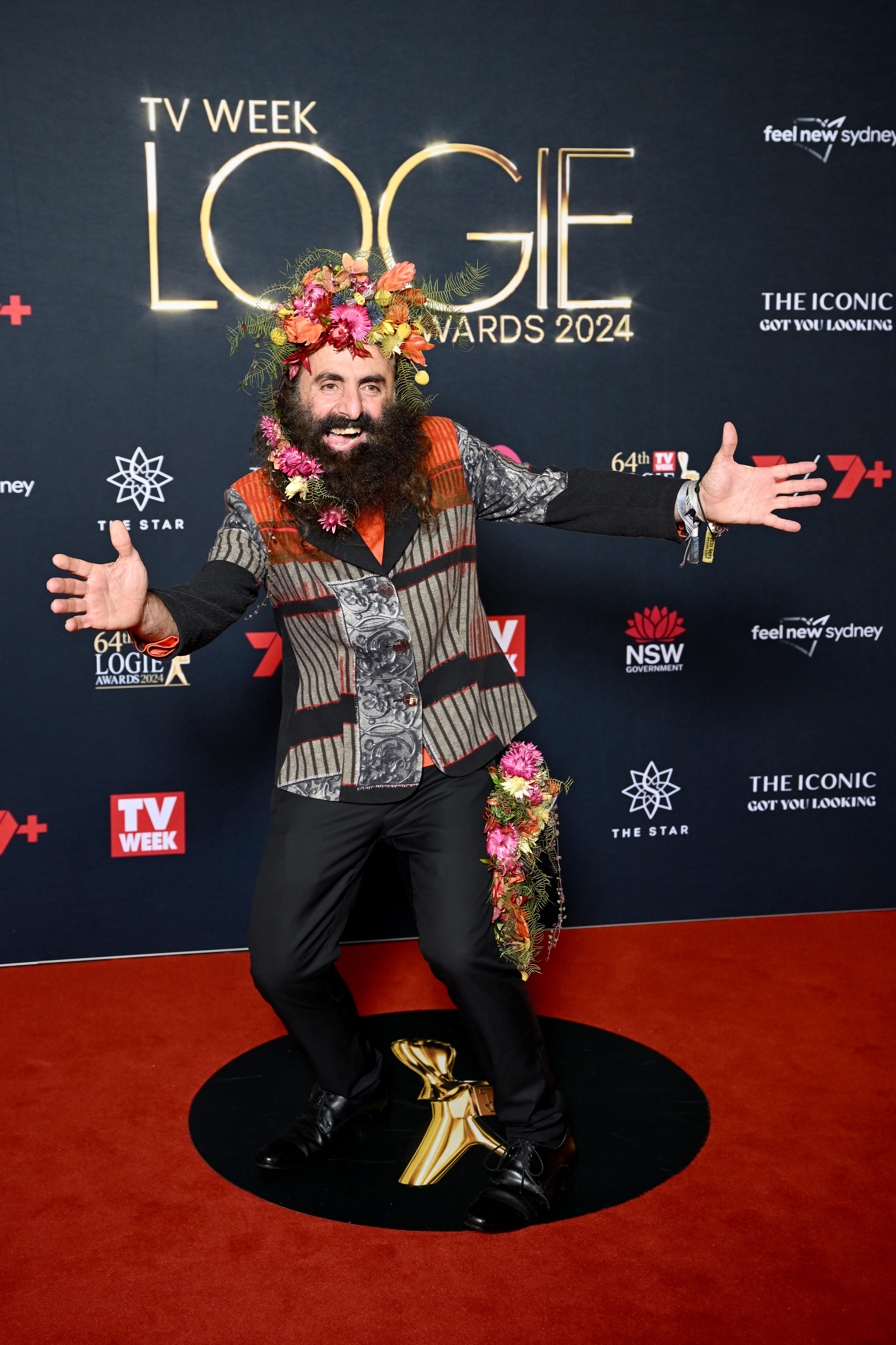 Georgiadis wears a flower crown, with extra blooms woven into his beard, and a striped patchwork blazer