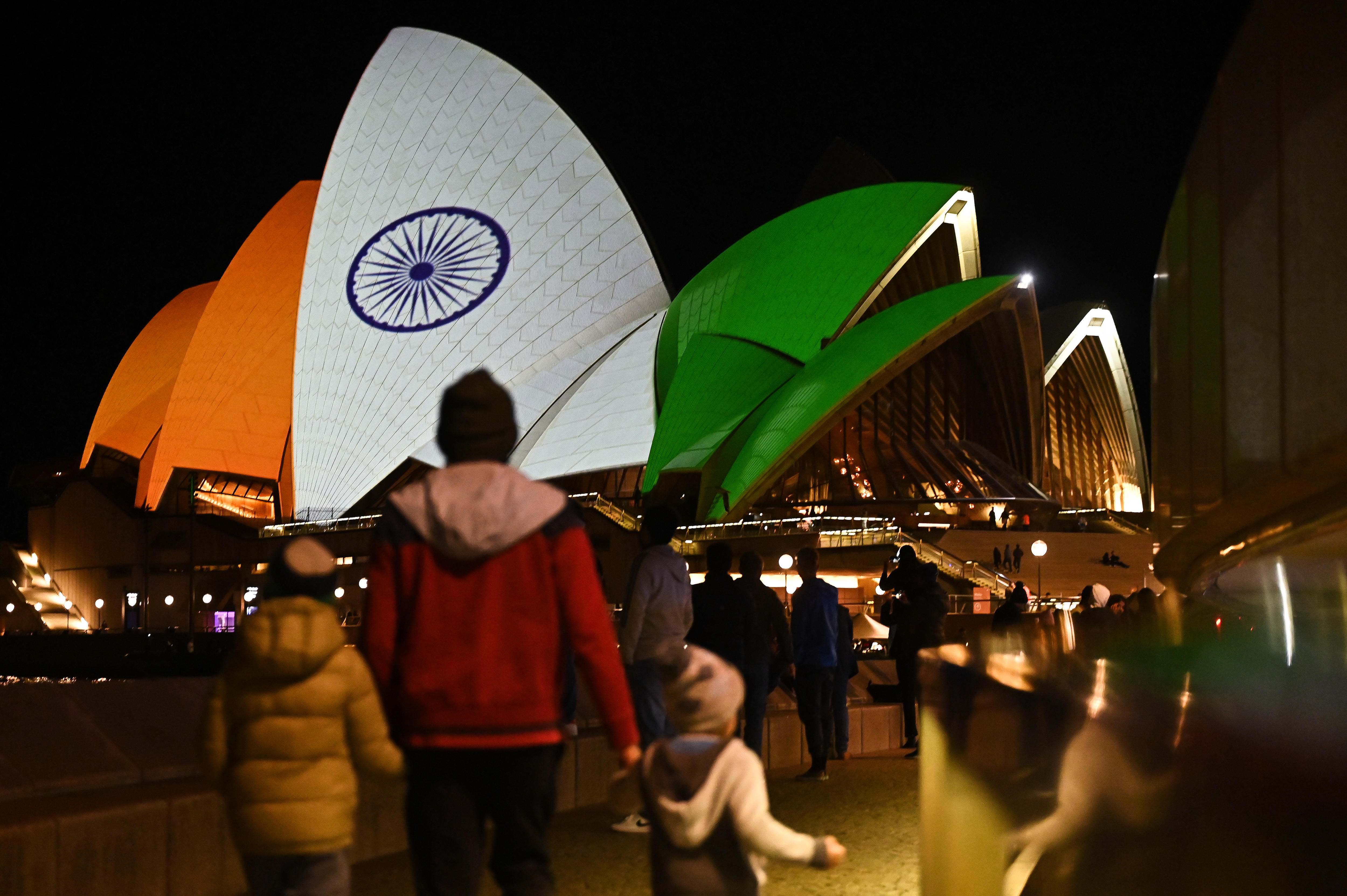 People walk outside a building at night time illuminated in orange, white and green.