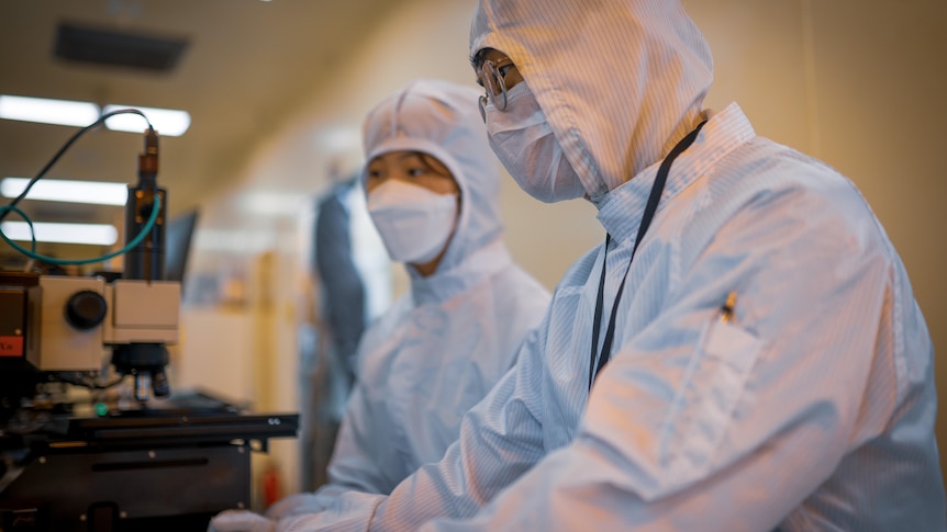 Two Koreans in full PPE examining factory equipment 