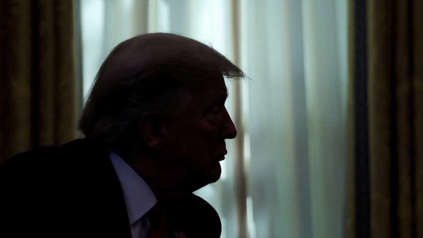 US President Donald Trump is silhouetted against a window in the Oval Office as he hosts Gilead Sciences